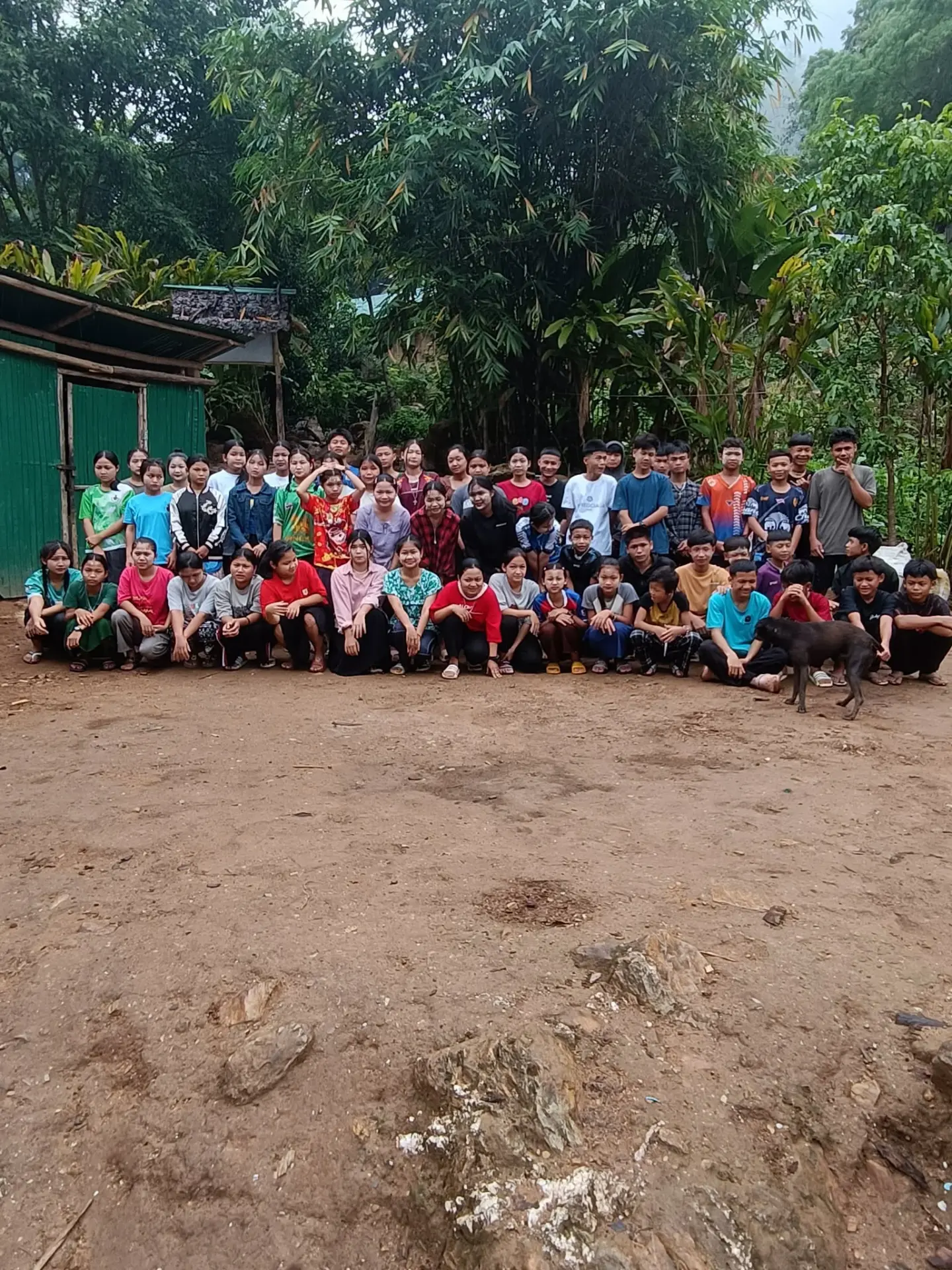 Holy Family mission youth gathered together in front of a village building