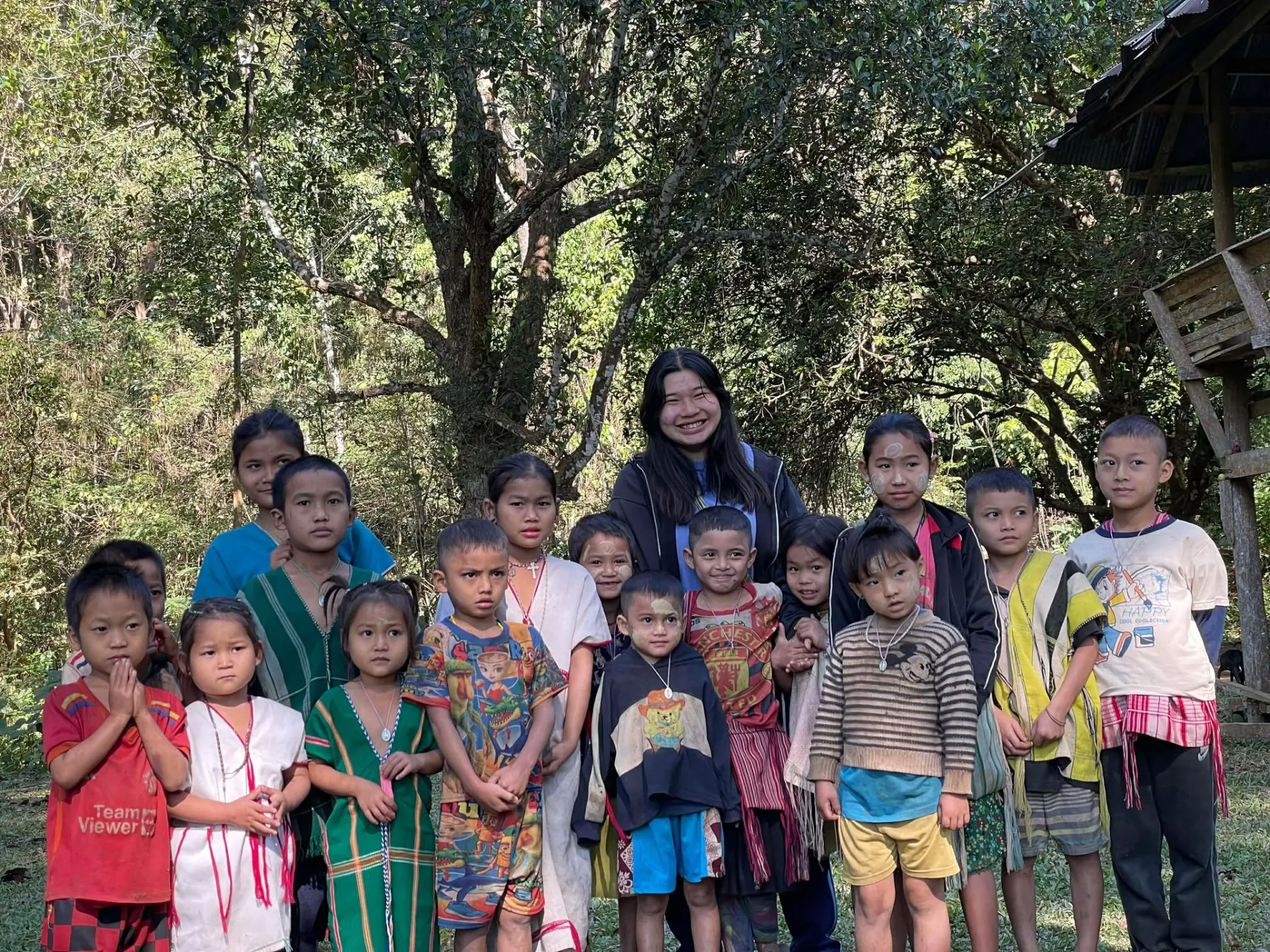 KACC visitor with a group of mission children under the trees in Myanmar