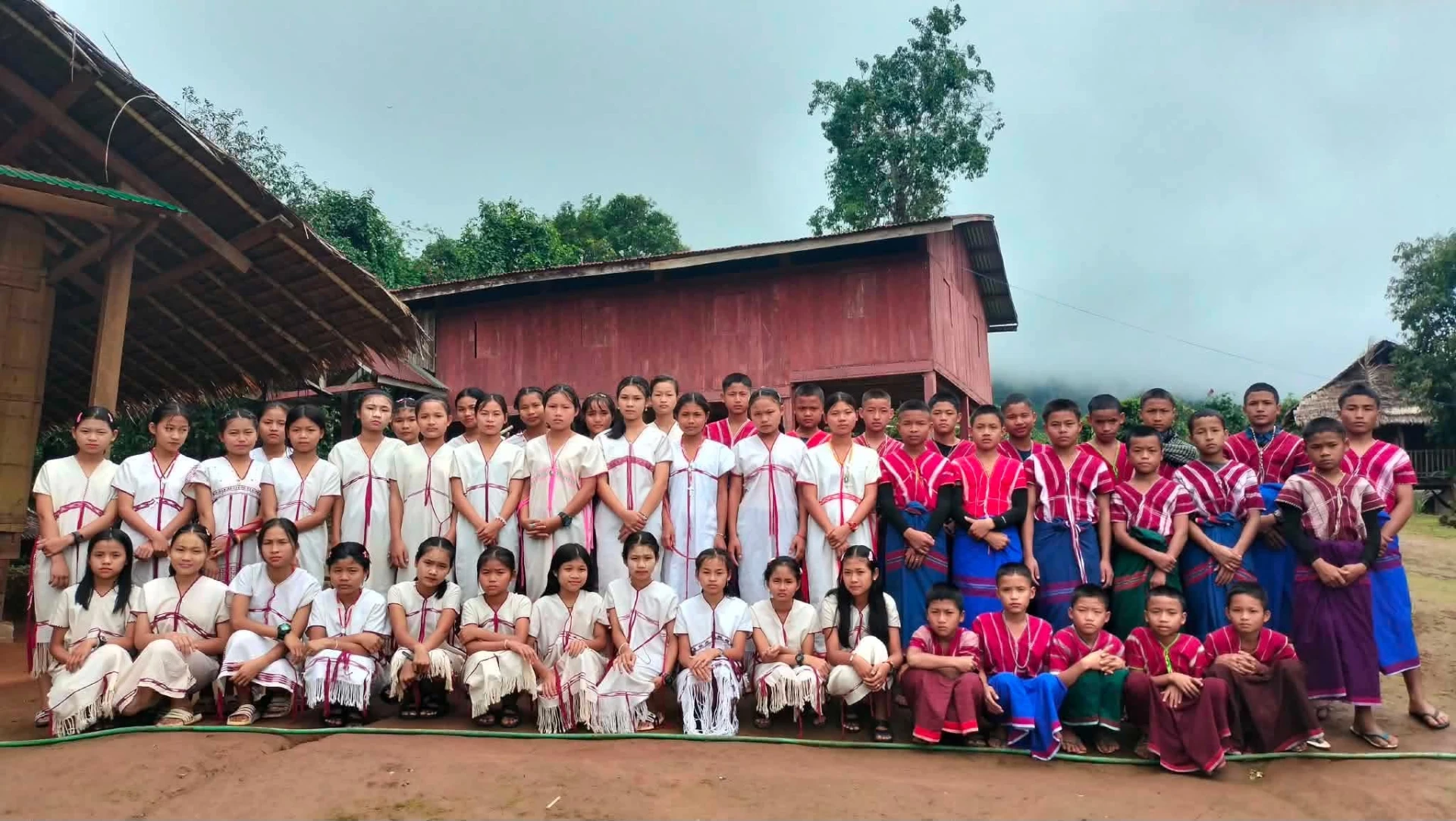 Sacred Heart mission children in traditional Karen dress in front of the village building